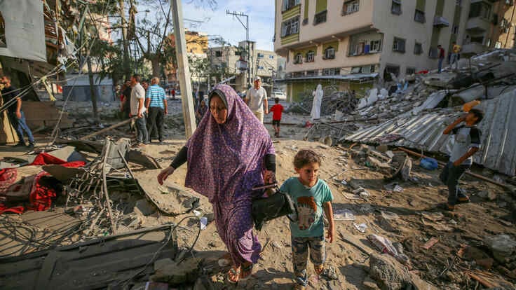 En mamma går med sitt barn genom ruinerna efter israeliska luftangrepp i Gaza den 7 oktober 2023.